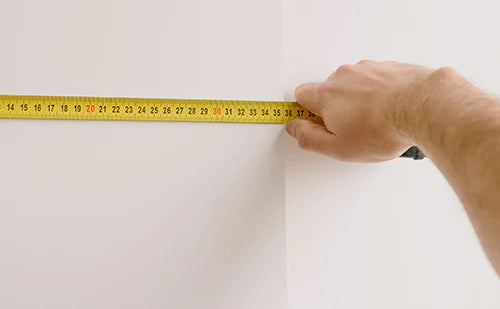 Image of a someone measuring a wall space for wallpaper with a measuring tape.