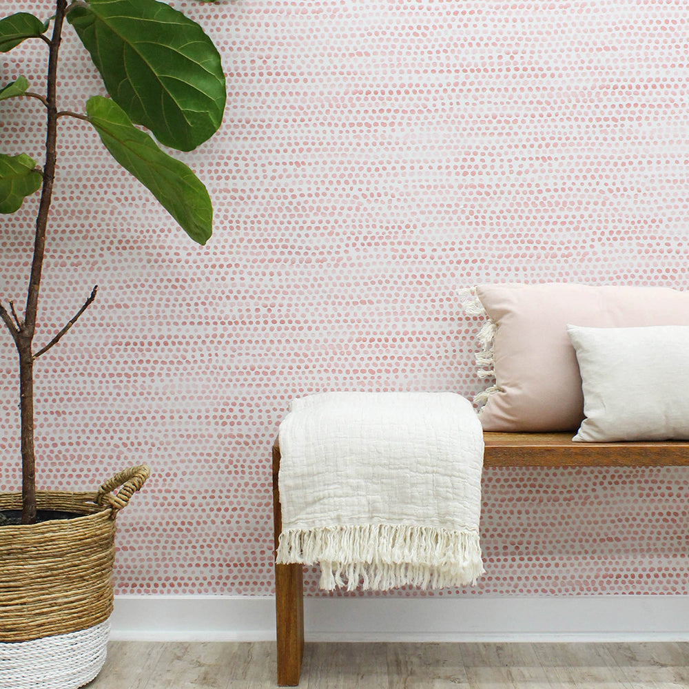 Moire Dots Removable Wallpaper - A wood bench with pillows and a white blanket in front of a wall featuring Tempaper's Moire Dots Peel And Stick Wallpaper in coral dots | Tempaper#color_coral-dots