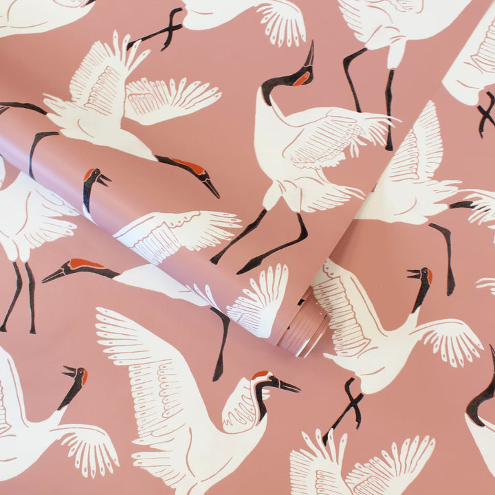 A roll of Tempaper's Family of Cranes Peel And Stick Wallpaper By Novogratz. #color_dusty-rose