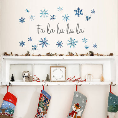 Tempaper's Fa La La La La Script Wall Decal shown above stockings and a shelf.