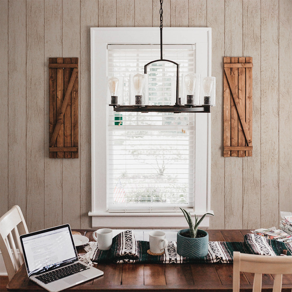 Tempaper's Farmhouse Planks Peel And Stick Wallpaper shown behind a table and chairs with a window in the middle.