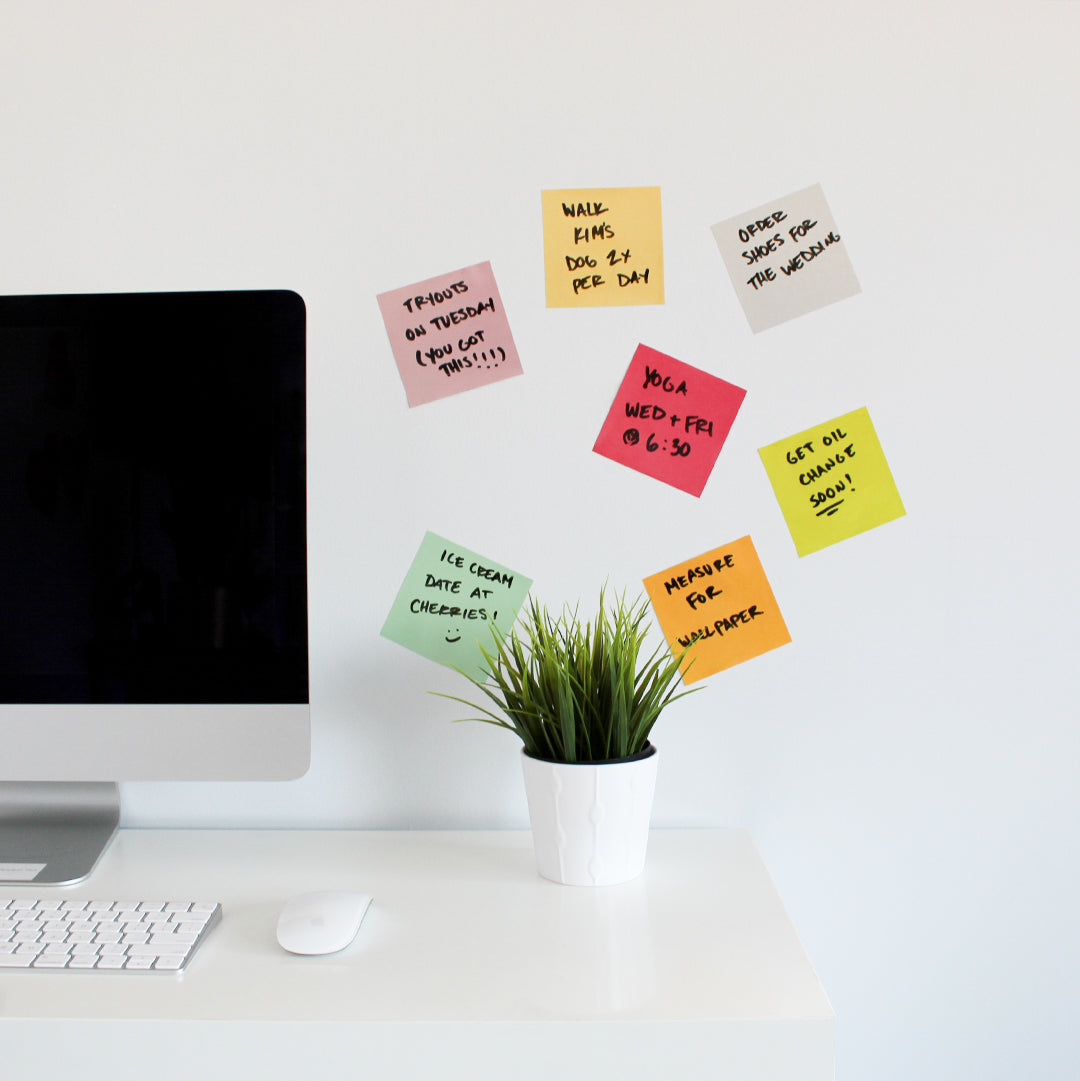 Tempaper's Dry Erase Sticky Notes Wall Decals shown above a desk behind a plant and computer monitor.