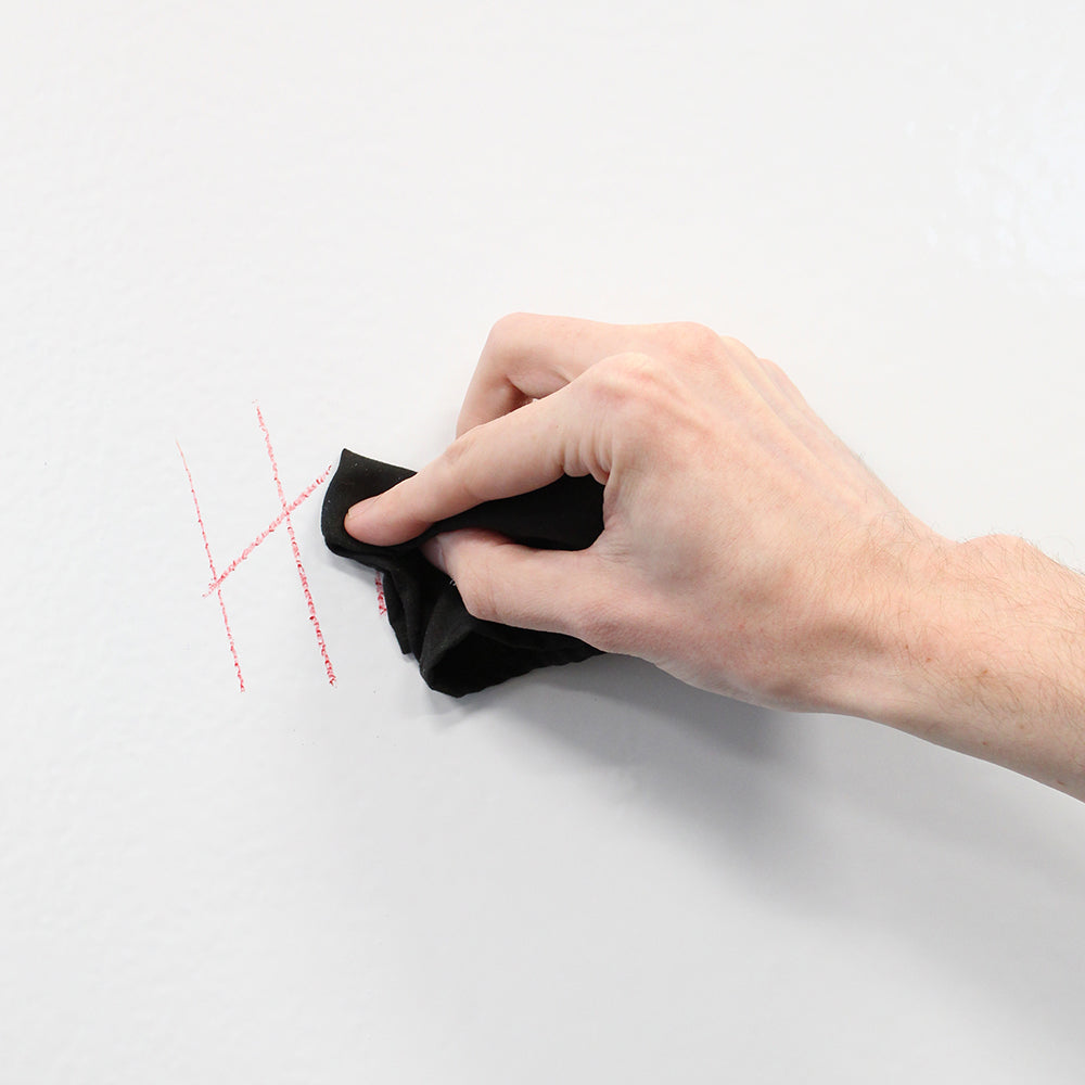 A hand erasing writing from Crayola's Dry Erase Crayons on a whiteboard.